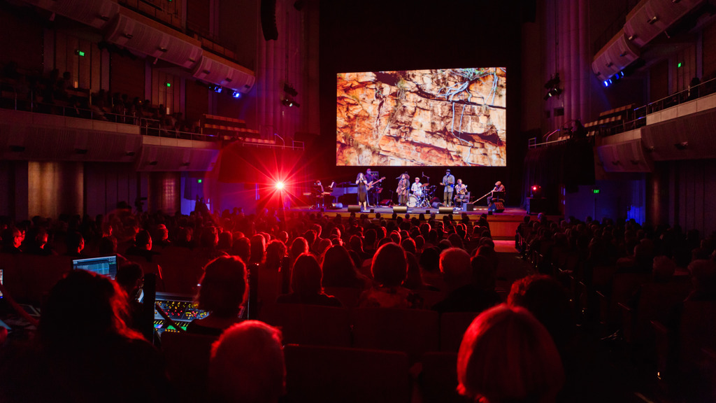 An ensemble performing on stage at City Recital Hall with projections and lighting effects overhead.