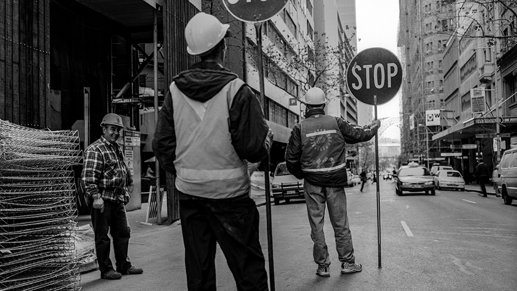 A black and white image of construction workers holding a stop sign on Pitt St, Sydney. Image courtesy of City of Sydney Archives, Tim Cole Collection.